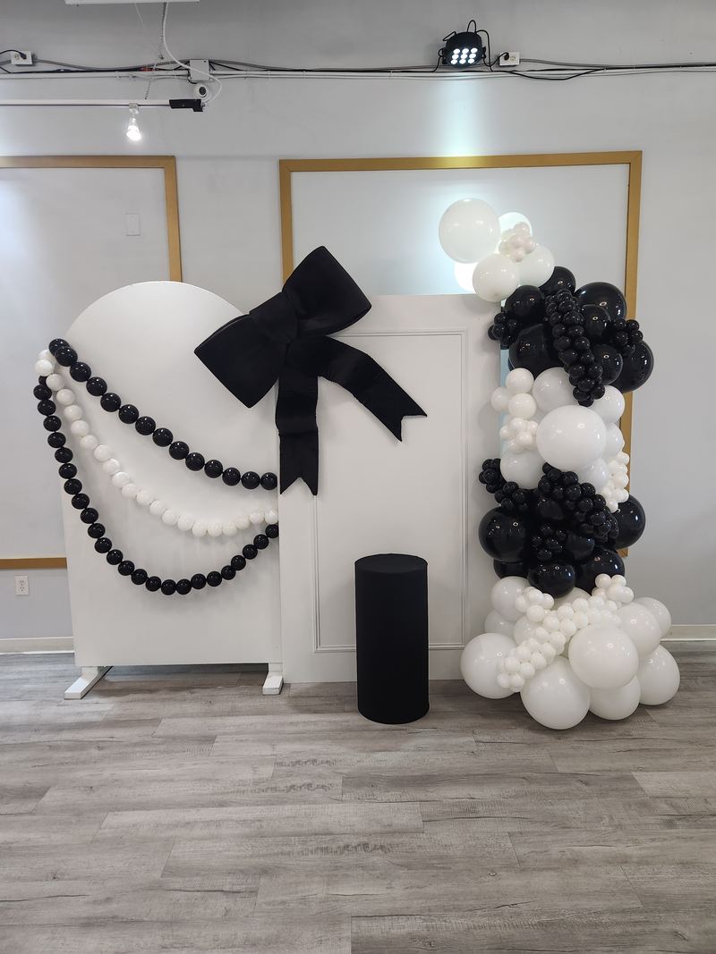 Fondo de arcos blancos con moño negro, hilos de perlas y globos negros y blancos