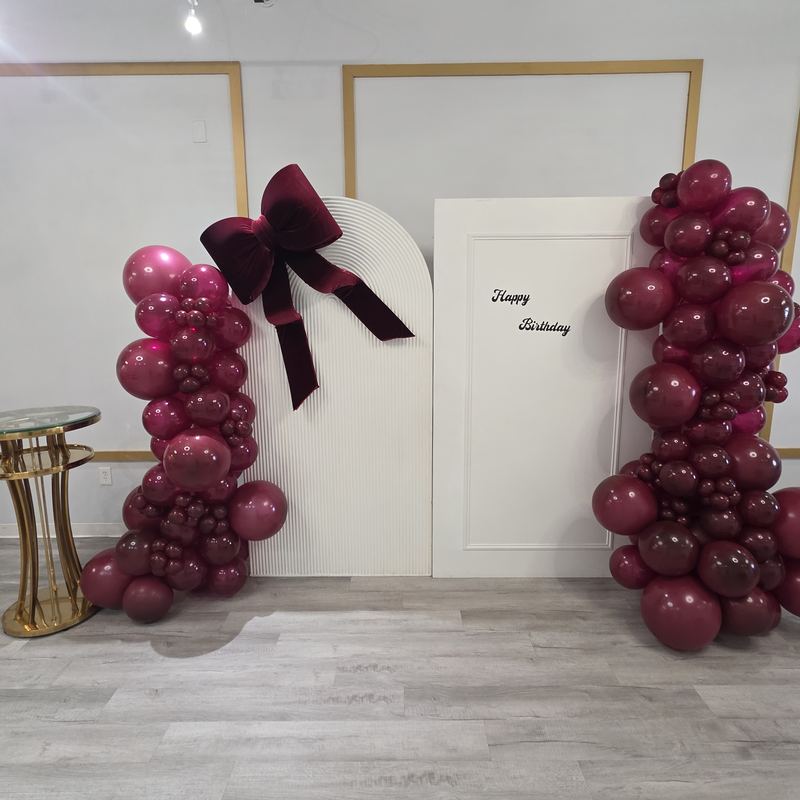 Columnas de globos color vino y un moño de terciopelo junto a un fondo blanco de Happy Birthday
