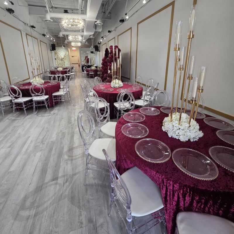 Mesas con manteles de terciopelo color vino, candelabros dorados altos, centros de mesa de flores blancas y lámparas de cristal