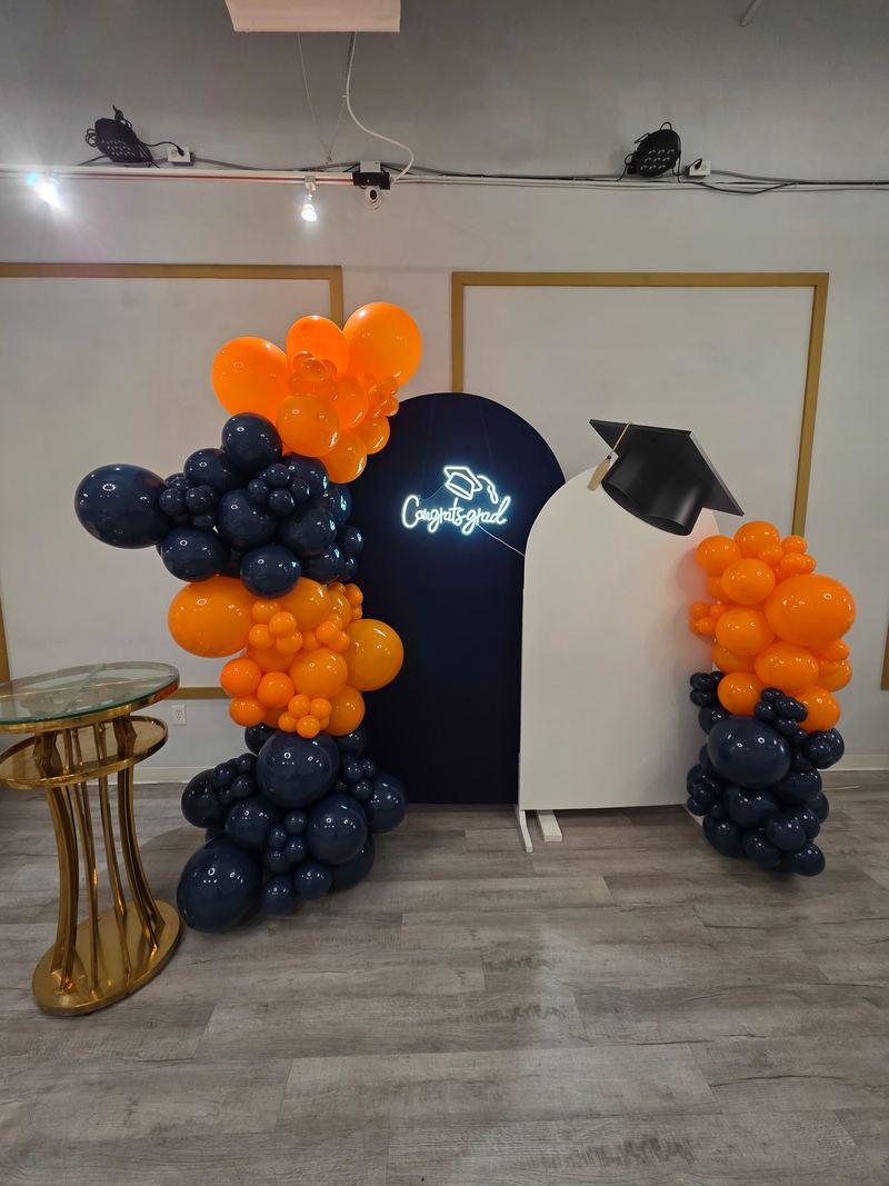 Fondo de graduación con arco azul marino, letrero de neón “Congrats grad”, birrete y globos azul marino y naranjas