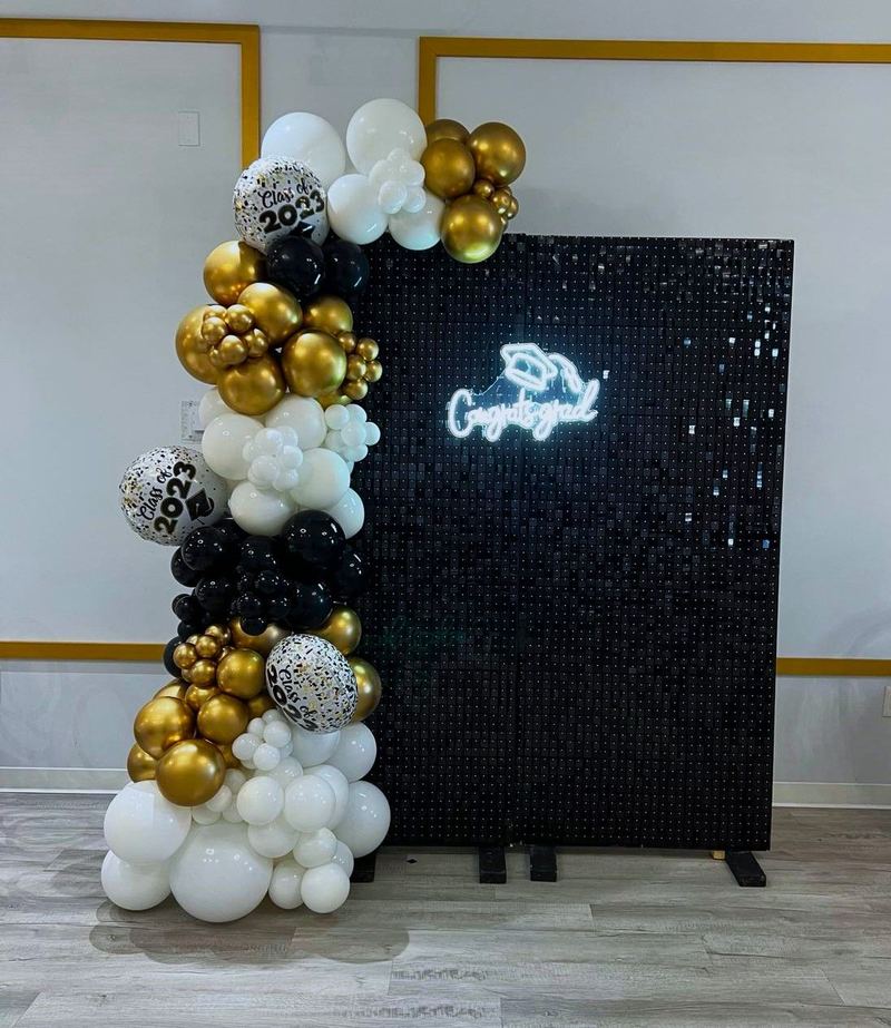 Pared de lentejuelas negras con letrero de neón “Congrats” y globos negros, dorados y blancos