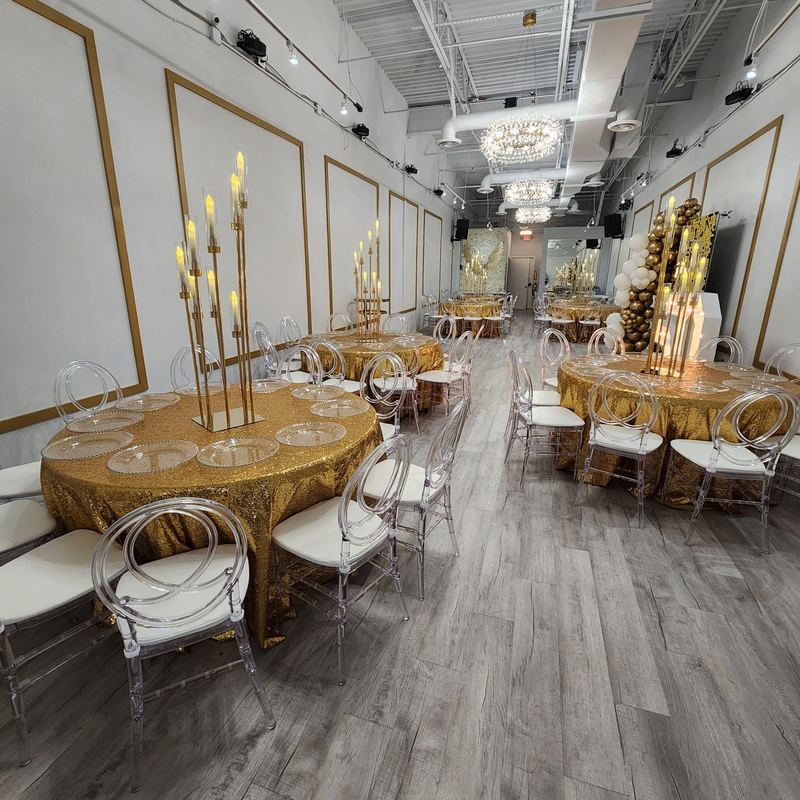 Mesas con manteles dorados de lentejuelas y candelabros dorados altos a lo largo del salón bajo lámparas de cristal