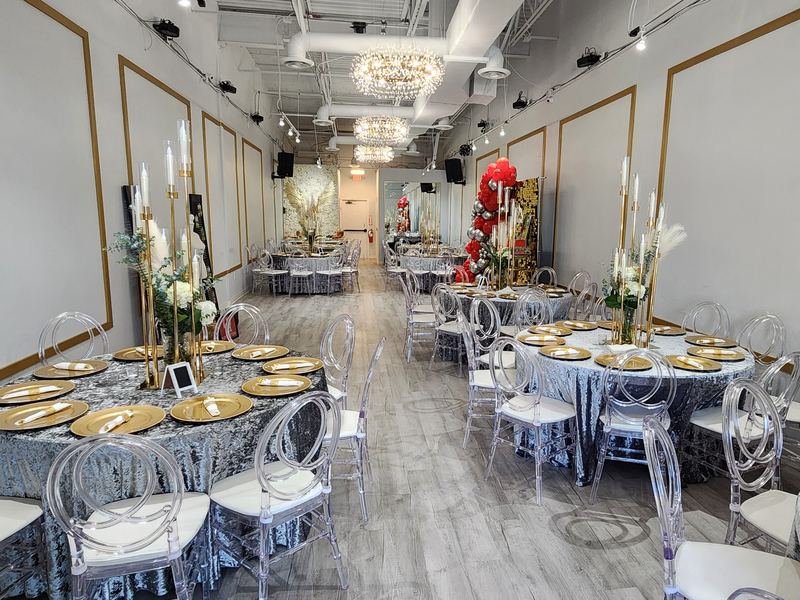 Mesas redondas con centros de mesa altos de candelabros dorados, flores blancas y platos base dorados bajo lámparas de cristal