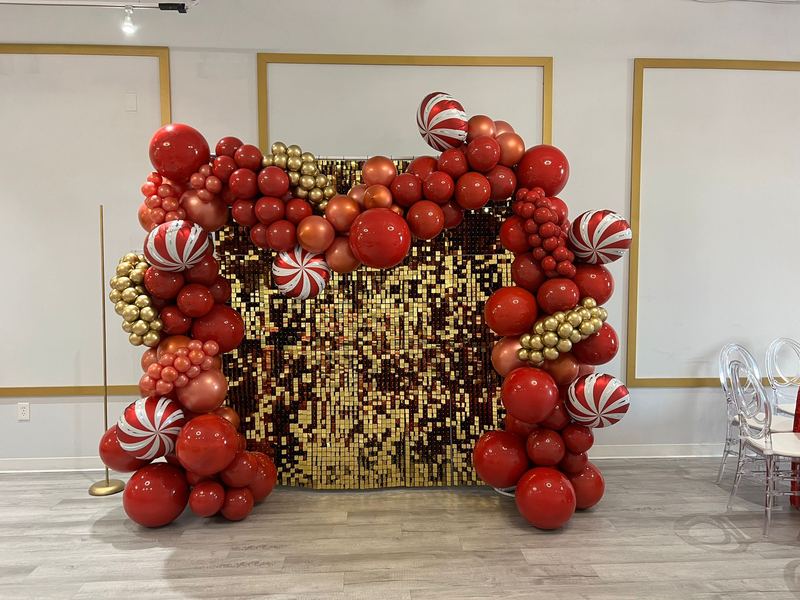 Pared navideña de globos rojos y dorados con dulces de menta y lentejuelas doradas