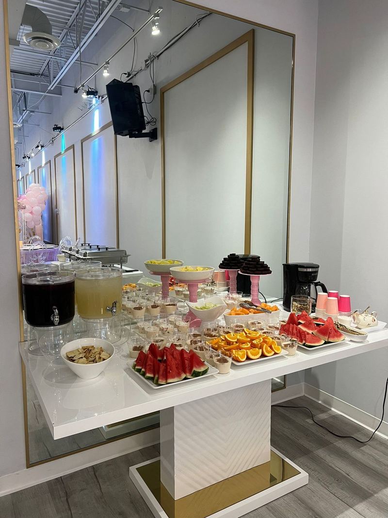 Mesa de buffet con charolas de fruta, postres y dispensadores de bebidas