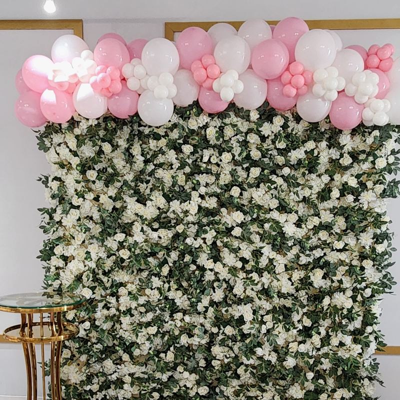 Guirnalda de globos rosas y blancos sobre una pared de rosas blancas y follaje