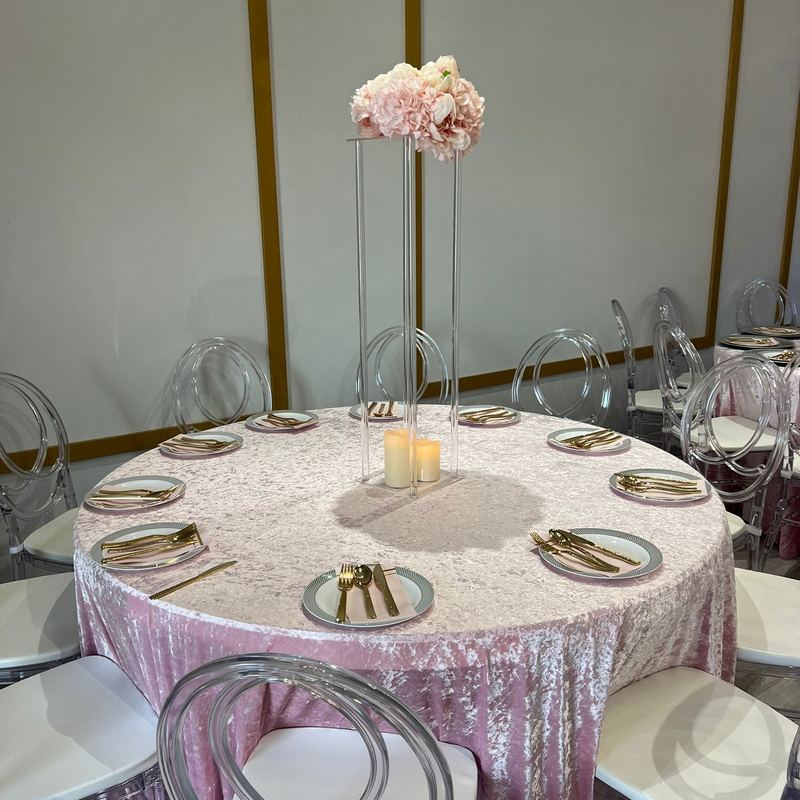 Mesa redonda con mantel de terciopelo rosa, cubiertos dorados y un centro de mesa alto de rosas rosas