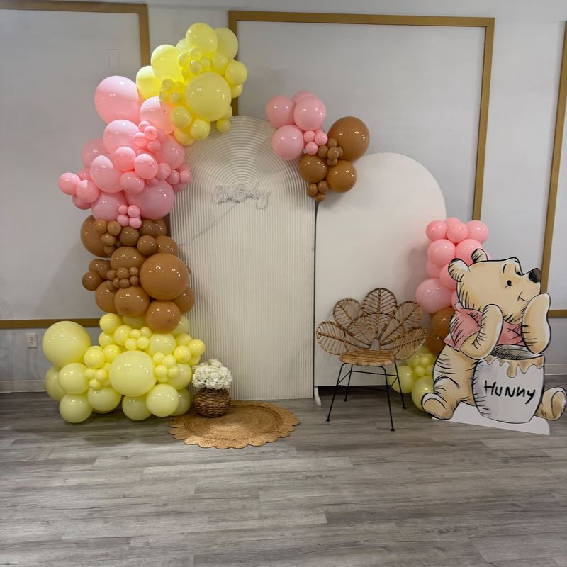 Winnie the Pooh baby shower backdrop with pink, yellow and brown balloons, an Oh Baby sign and a full Winnie the Pooh and honey pot cutout