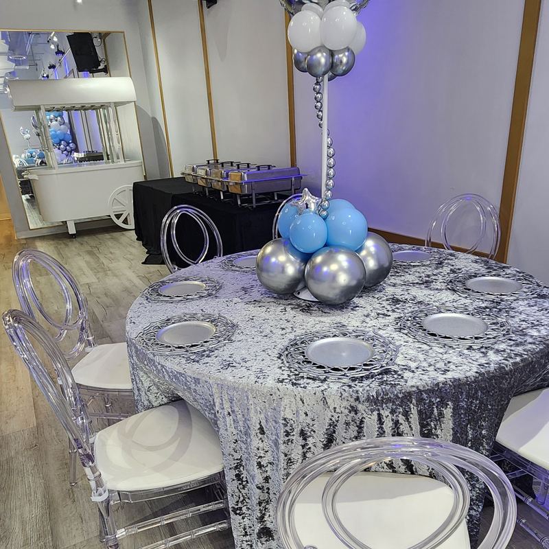 Mesa con mantel de terciopelo plateado y centro de mesa de globos con luna creciente bajo luces azules y moradas