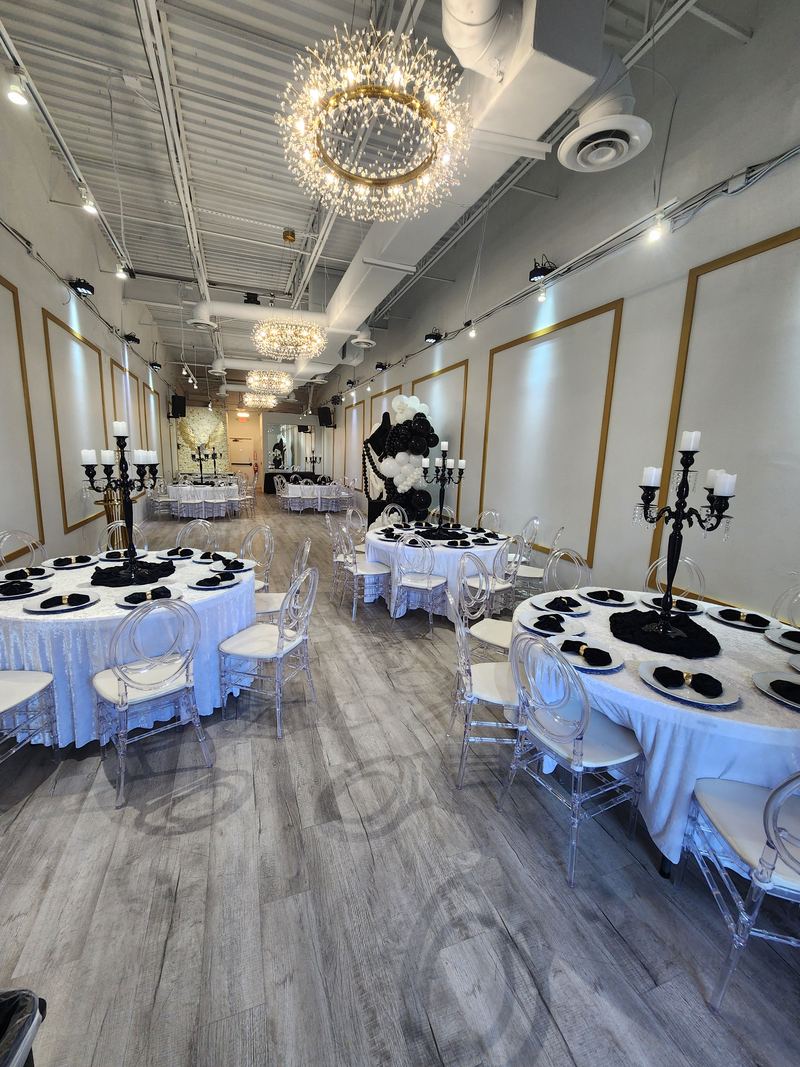 Round tables with white linens, black charger plates and black candelabras under crystal chandeliers